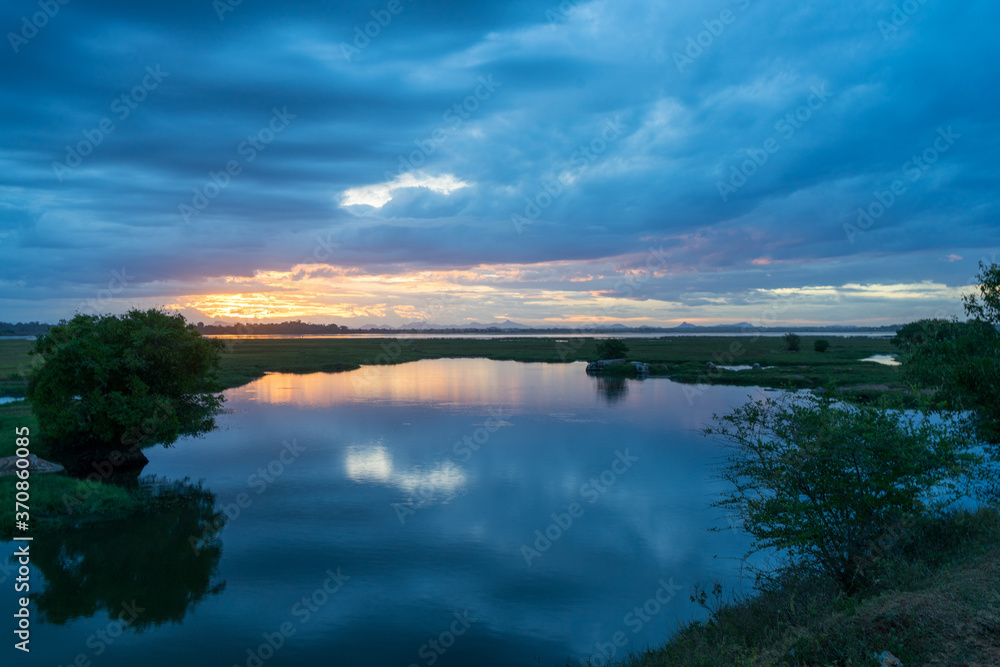 Fototapeta premium Storm clouds over the water with the sunset over the lake. Orange sunlight, dramatic sky with clouds. Beautiful reflections in water