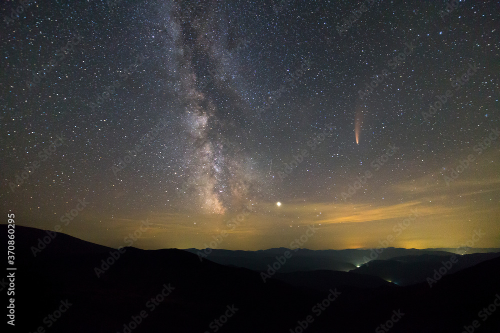 Fototapeta premium Night landscape of mountains with stars covered sky and Neowise comet with light tail.