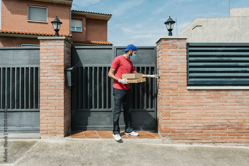 Male postal worker using intercom while standing with package at house gate Male postal worker using intercom while standing with package at house gate