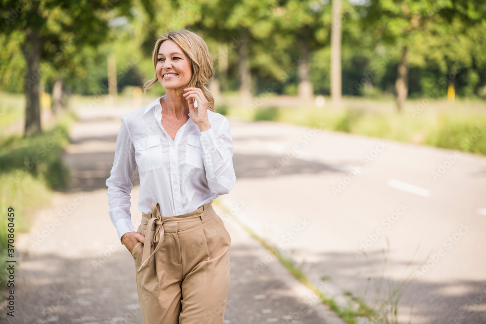Thoughtful mature businesswoman smiling while standing on road Thoughtful mature businesswoman smiling while standing on road