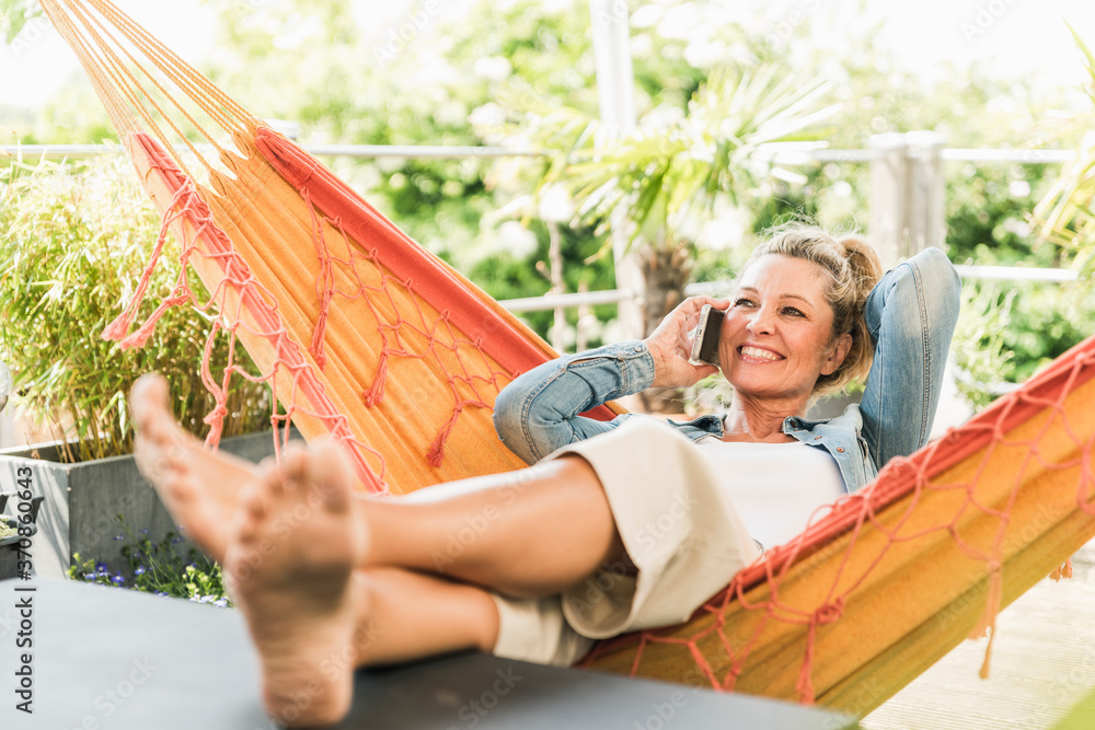 Portrait of happy mature woman on the phone relaxing in hammock on ...