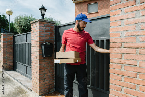 Wallpaper Mural Bearded delivery person standing with packages against house gate on sunny day Torontodigital.ca
