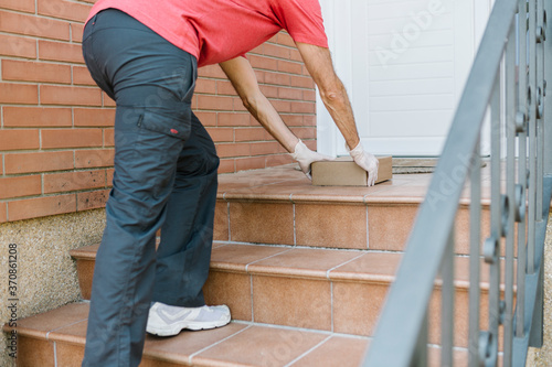 Low section of male postal worker delivering package at front door during pandemic