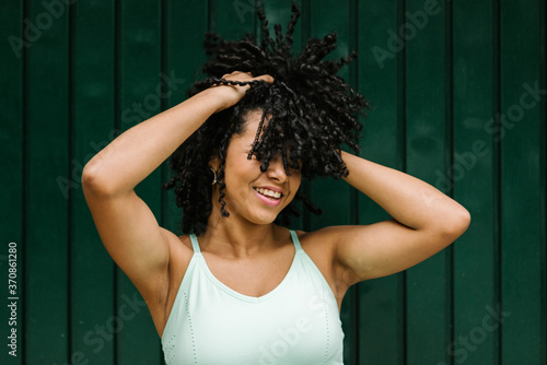 Happy young woman with hand in black curls while standing against green metal door photo