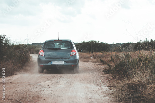 Small grey hatchback driving on dirt roads on the island of Brac, Croatia. Driving between olive trees and rocks on small paths, throwing dust behind it. Seen from the car behind following it © Antonio