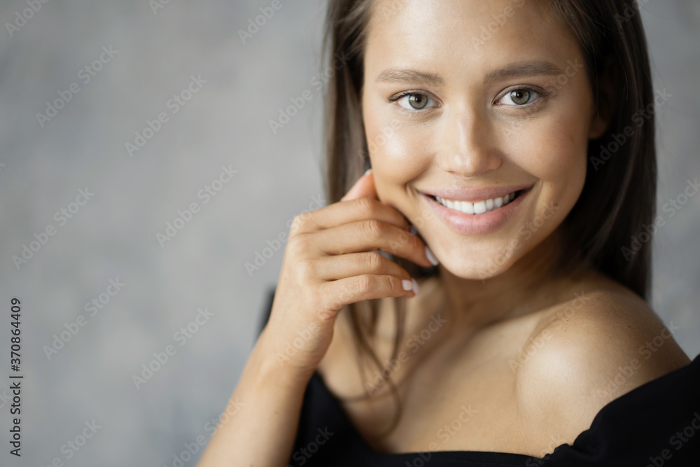 a happy girl with a pleasant smile in a black jacket poses for a photographer on a gray background a happy girl with a pleasant smile in a black jacket poses for a photographer on a gray background