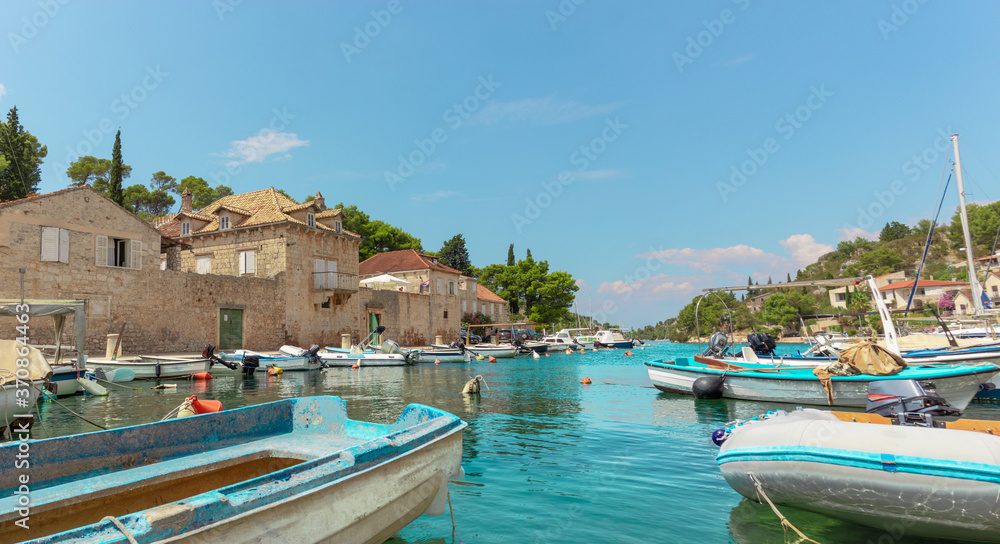 Waterfront view of a tiny village of Bobovisca on the island of brac. Crystal clear teal and green water reflection the bright sky. Small boats docked in the harbour