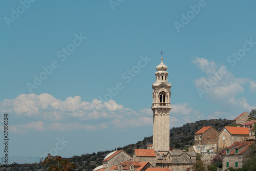Tall belltower in a tiny village of Lozisca on the island of Brac, Croatia. Beautiful christian tower rising above the old buildings