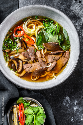 Pho Bo  Vietnamese fresh rice noodle soup with beef, herbs and chili. Black background. Top view