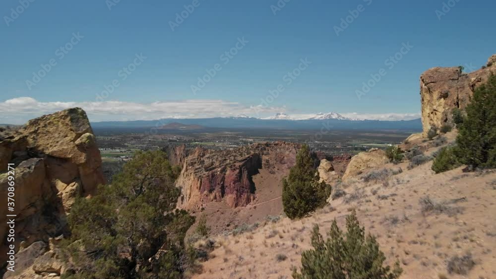 Aerial drone flight high over through orange and red desert dry rock cliffs mountain range in background blue sky sunny day at smith rock state park Terrebonne central oregon pacific northwest usa Aerial drone flight high over through orange and red desert dry rock cliffs mountain range in background blue sky sunny day at smith rock state park Terrebonne central oregon pacific northwest usa