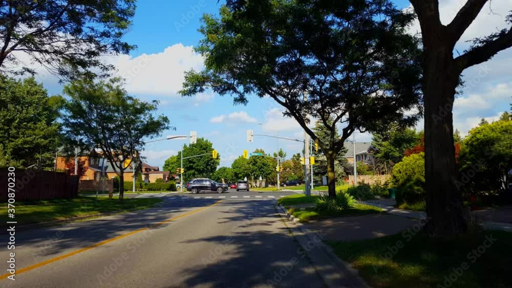 City Suburb Light Intersection With Driving Traffic in Summer. Urban Suburban Vehicles Drive Through Traffic Light Intersection During Day. City Suburb Light Intersection With Driving Traffic in Summer. Urban Suburban Vehicles Drive Through Traffic Light Intersection During Day.