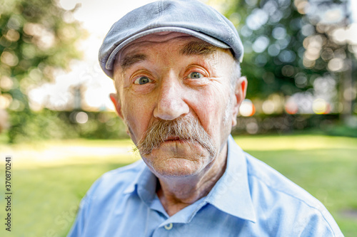 Portrait of smiling senior man with white mustache looking at camera against green grass and smiling. soft focus