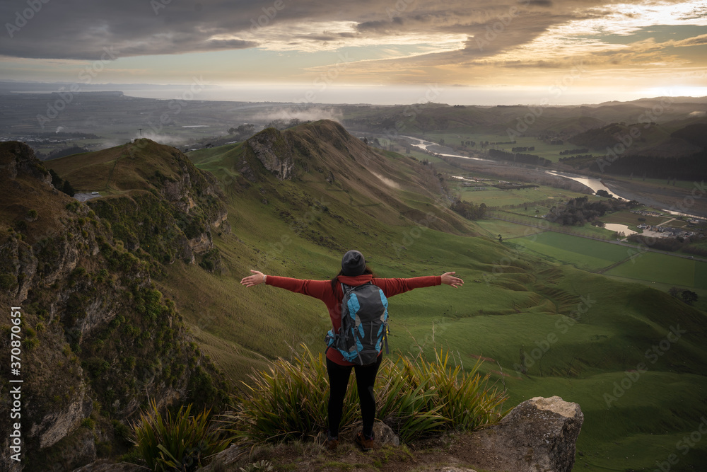 Fototapeta premium Young woman with backpack opening her arms at the top of Te Mata Peak, Hawke's Bay. New Zealand