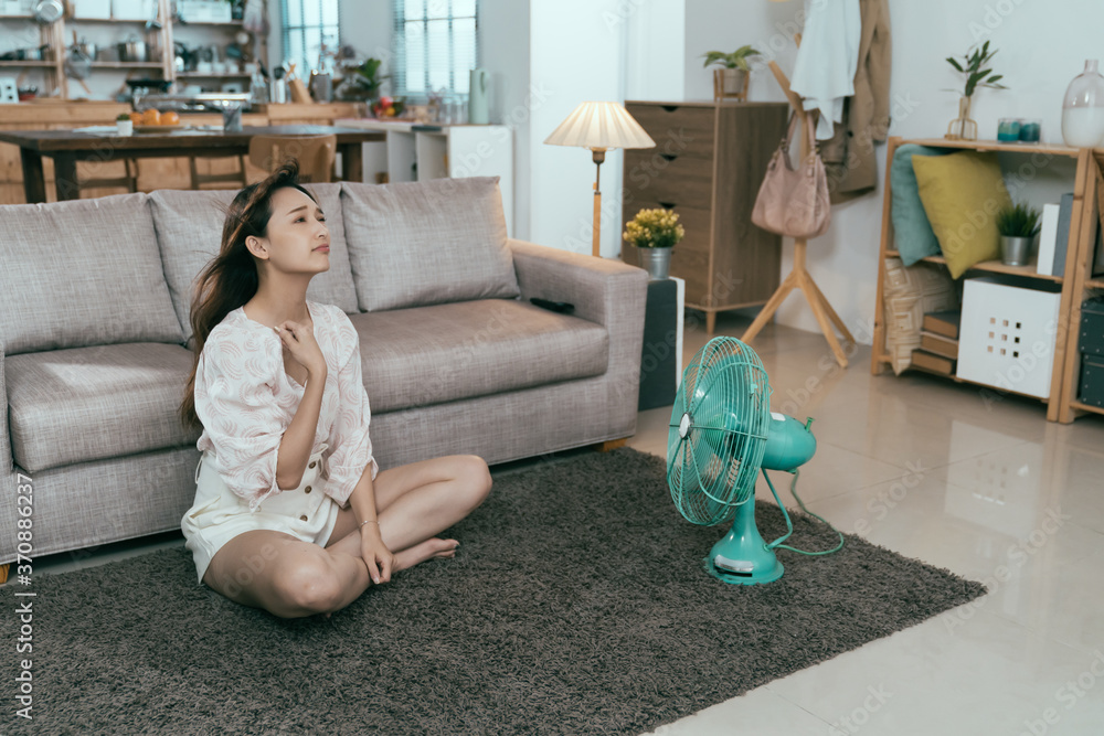 © PR Image Factory - asian young female feeling suffocated tries to blow away heat with electric fan. sweaty chinese lady seated in front of table fan pulling shirt is still hot.