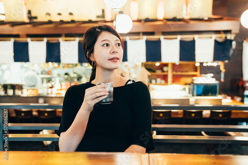Portrait of happy young asian korean woman with traditional cup in hands drinking hot matcha tea in restaurant. elegant beautiful lady looking aside while enjoy beverage in japanese meal store.