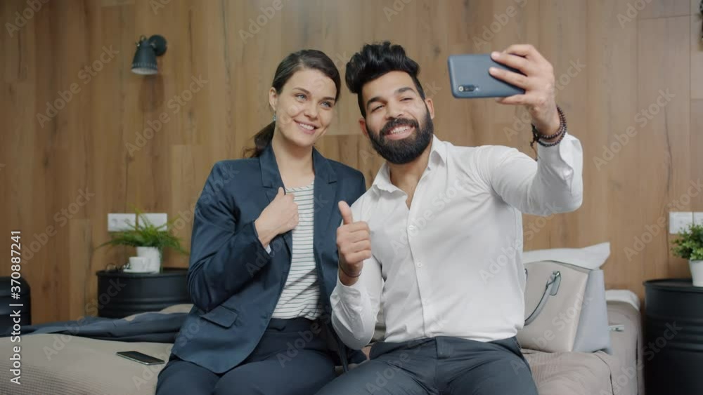 Man and woman colleagues are taking selfie in hotel room posing for smartphone camera having fun together. Commuting, people and devices concept. Man and woman colleagues are taking selfie in hotel room posing for smartphone camera having fun together. Commuting, people and devices concept.