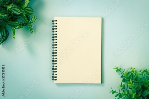 Spiral Notebook or Spring Notebook in Unlined Type and Office Plants at Top Left Corner and Bottom Right Corner on Blue Pastel Minimalist Background in Vintage Tone