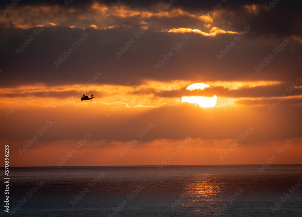 A Blackhawk helicopter banking left awawy from the sun during a training mission at sunset 