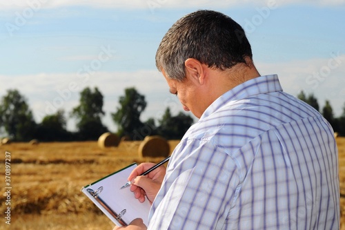 Farmer agronomist examines the field where the crop is harvested and makes notes in his notebook