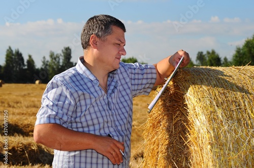 Farmer agronomist examines the field where the crop is harvested and makes notes in his notebook