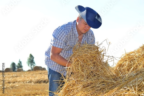Man cowboy in hat on the farm is doing work and collecting hay