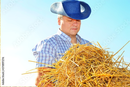 Man cowboy in hat on the farm is doing work and collecting hay