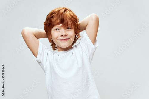 Red-haired boy holds hands behind his head smile white t-shirt studio