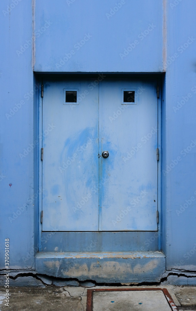 The weathered blue door on cracked cement base