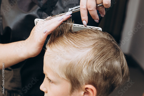 Hair cutting with scissors. Blonde boy at the barbershop. High quality photo