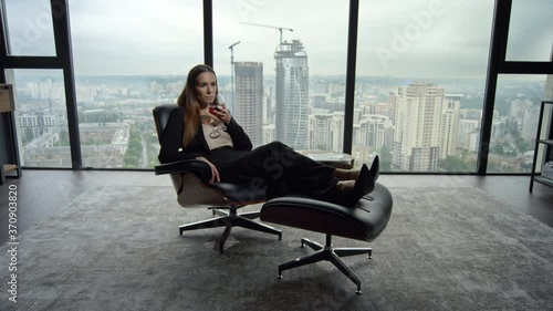 Businesswoman relaxing on chair in office. Woman smelling aroma of wine in glass photo