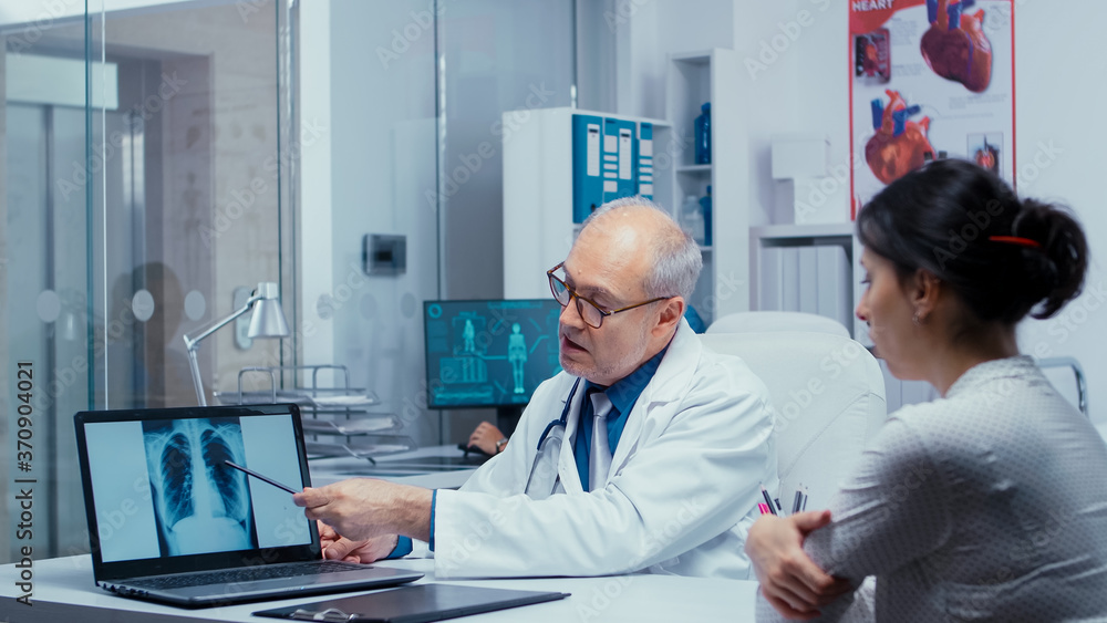 Obraz premium Discussing lungs X Ray result with young female patient. Elderly senior experienced doctor talking with patient about lungs, x ray pneumonia, cancer, examination specialist consulting diagnosis in