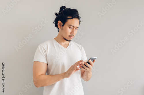 Long hair Asian man in white casual t-shirt is using smartphone.