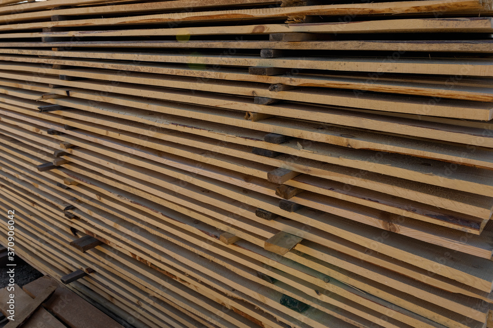 Long wooden planks for construction works in the sawmill. Timber mill. Raw wood beam, stacked at construction site. Long wooden planks for construction works in the sawmill. Timber mill. Raw wood beam, stacked at construction site.