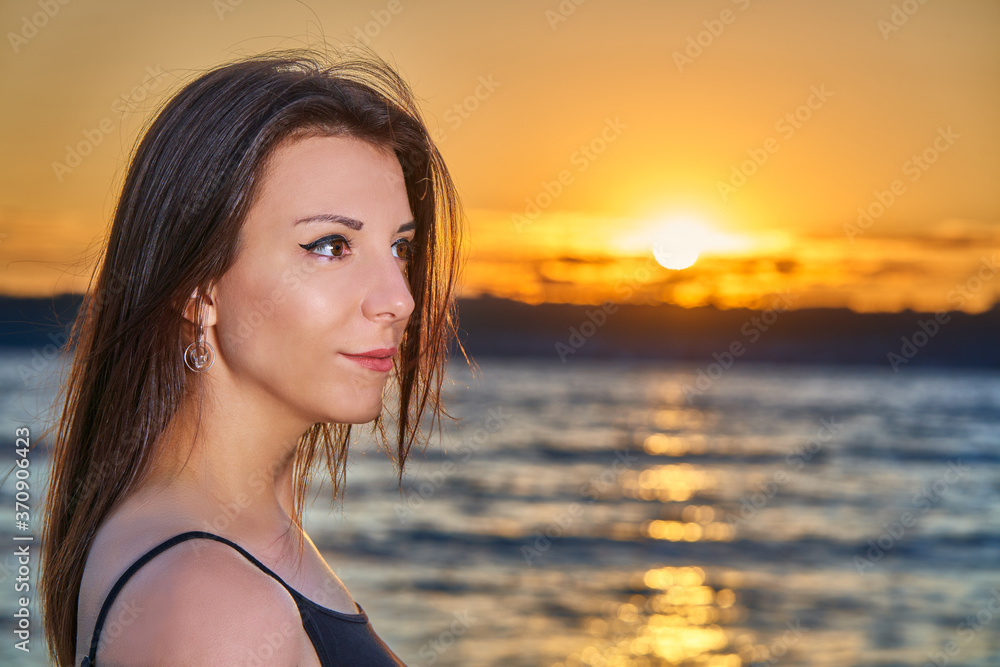 Portrait of a young brunette girl against the backdrop of the sunset over a large lake. Close-up of the girl's face.