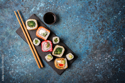 Set of sushi rolls served on a black slate board with chopsticks