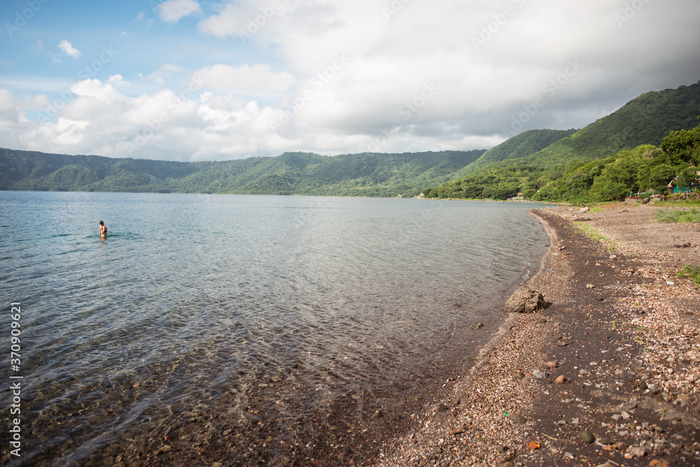 shore of Laguna de Apoyo lake in inactive volcano caldera surrounded by jungle and tourist in the water