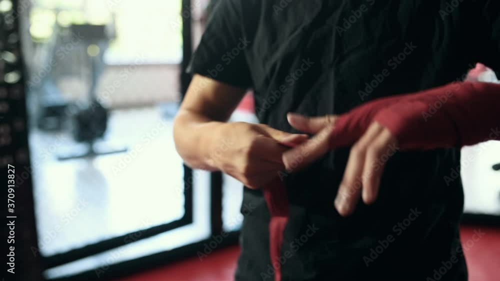 Guy stands indoors and wraps hand by boxing bandage. Guy stands indoors and wraps hand by boxing bandage.