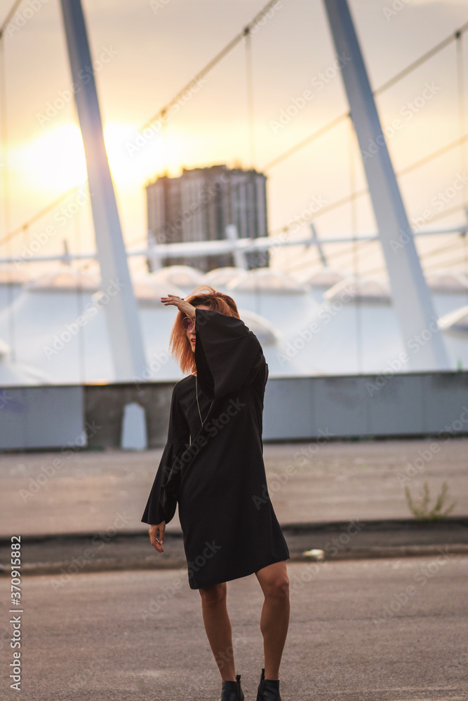 Obraz premium Creative redhead woman in black dress in the city on sunset.