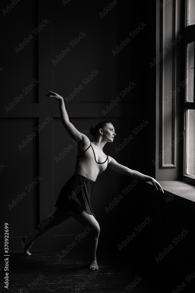 Beautiful young female classical ballet dancer on pointe shoes wearing a black leotard and skirt on a brick background
