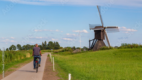 Fotografie Tourist passing Windmill the Monnikenburenmolen or Nijhuizumermolen a drainage mill in Nijhuizum, Friesland, Netherlands