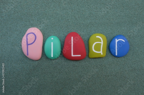 Pilar, feminine Spanish language given name composed with handmade multicolored stone letters over green sand