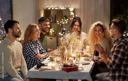 holidays and celebration concept - happy friends having christmas dinner at home with bottle of non-alcoholic red wine