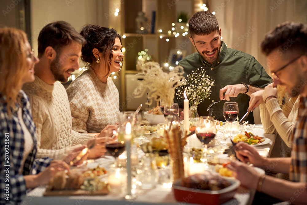 holidays, celebration and people concept - happy smiling friends having christmas dinner party at home in evening