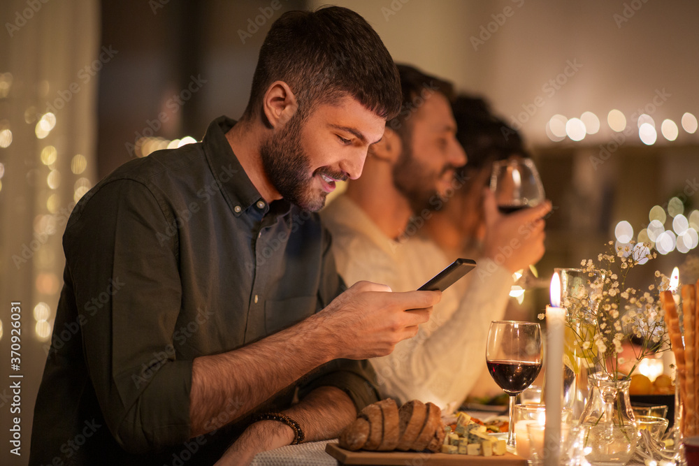 holidays and people concept - man with smartphone at dinner party with friends at home