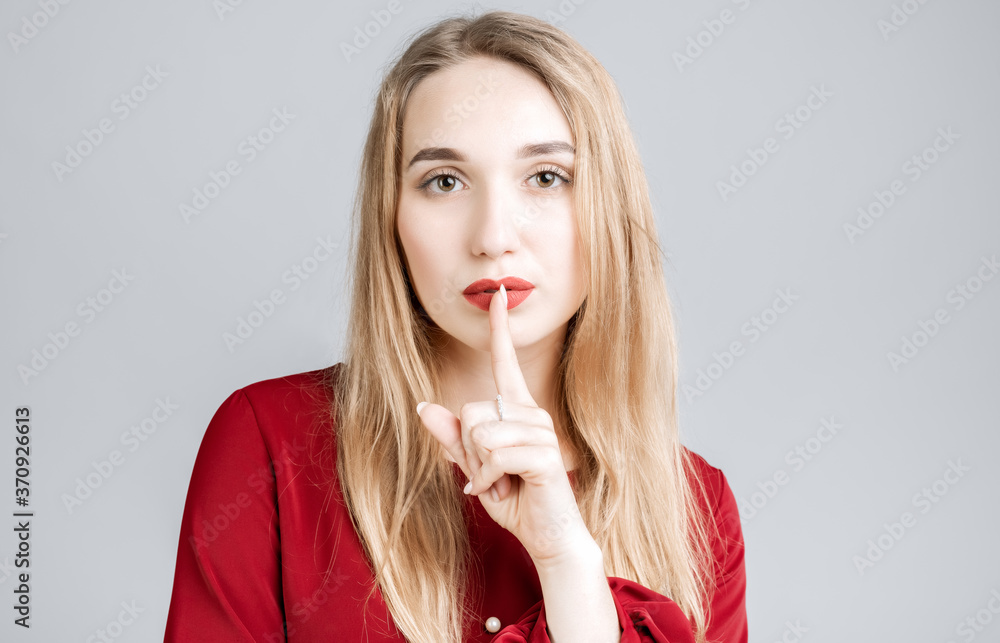 Emotional European young woman with long blonde hair dressed in casual clothes, keeping index finger at her lips, saying Shh, Keep silent, It's secret. Emotional European young woman with long blonde hair dressed in casual clothes, keeping index finger at her lips, saying Shh, Keep silent, It's secret.