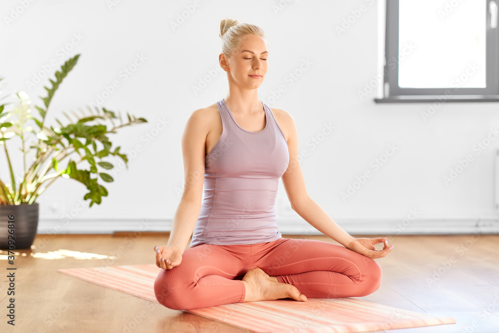 mindfulness, spirituality and yoga concept - happy young woman meditating in lotus pose at home