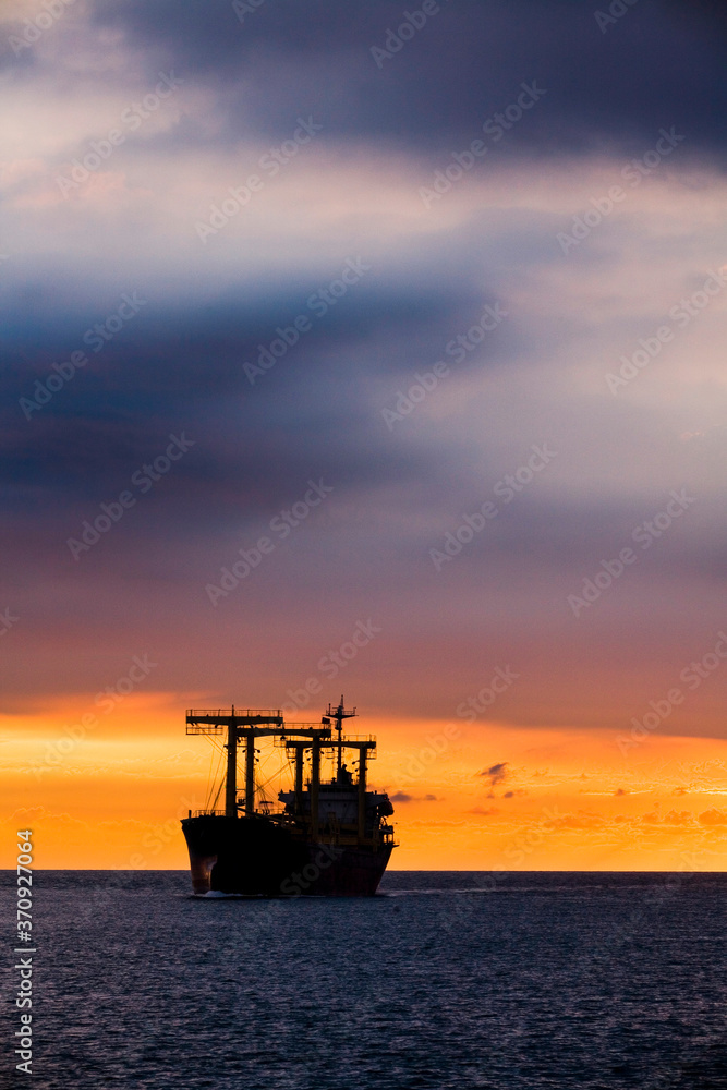 Sunset into the sea with the large ship silhouette.