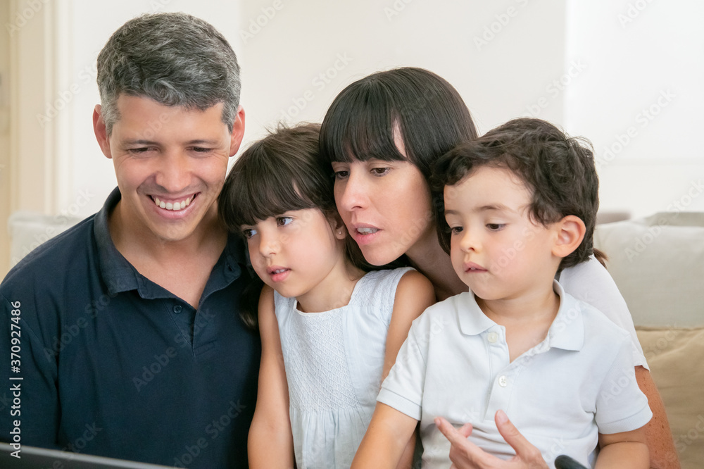 Happy parent and two kids looking at computer display, sitting on couch together. Medium shot. Communication or entertainment internet concept Happy parent and two kids looking at computer display, sitting on couch together. Medium shot. Communication or entertainment internet concept