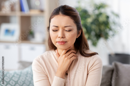 health, cold and people concept - sad sick young asian woman with sore throat at home photo