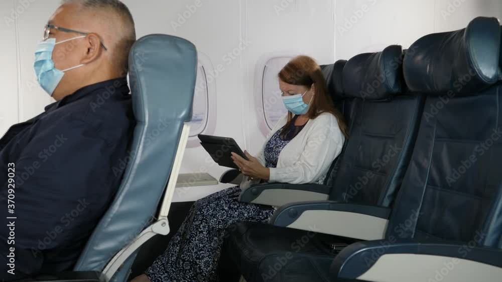 4K: Caucasian Female Airplane Passenger using a Digital Tablet wearing Face mask on plane journey. Air Travel. Tracking Shot. Stock Video Clip Footage 4K: Caucasian Female Airplane Passenger using a Digital Tablet wearing Face mask on plane journey. Air Travel. Tracking Shot. Stock Video Clip Footage